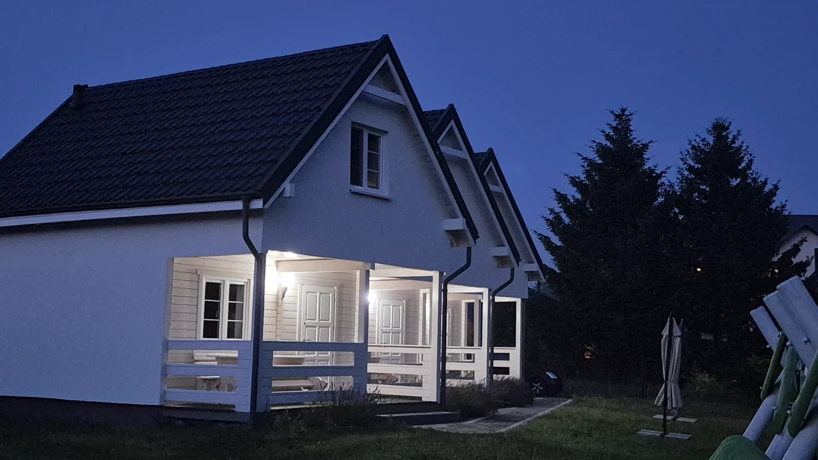Trzy domki aleChata oświetlone wieczorem, widok od strony ogrodu